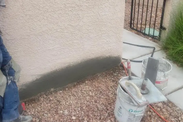 Exterior stucco patch & coat — Base-of-wall stucco repair and recoat along a side yard elevation.